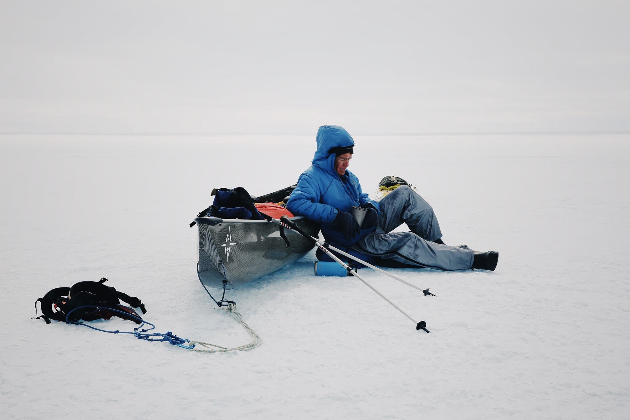Man in Parka Sitting on Ice beside a Canoe